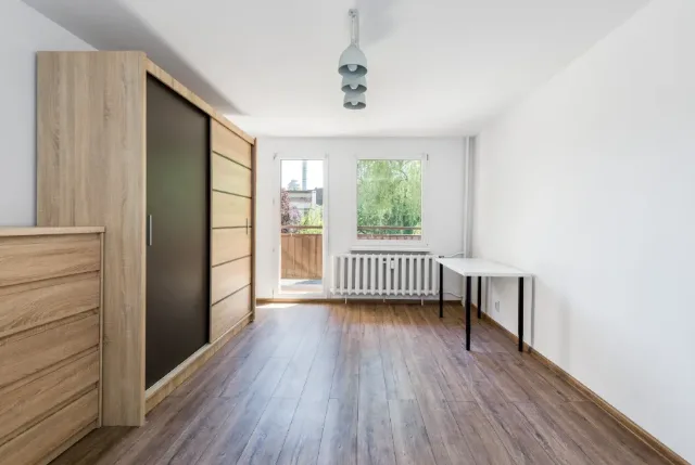 Pusty pokój z szafą przesuwną, panelami podłogowymi i wyjściem na balkon