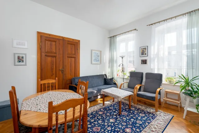 Salon w kamienicy z drewnianymi drzwiami dwuskrzydłowymi, szarą sofą, fotelami i granatowym dywanem