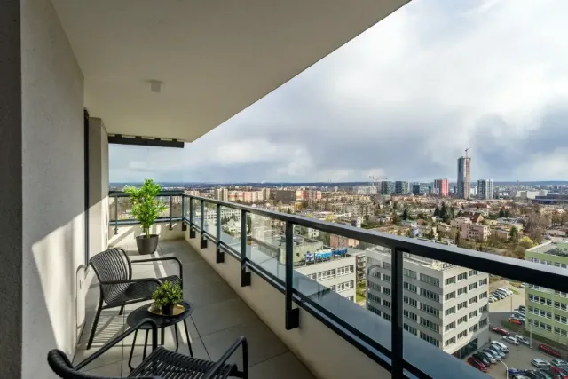 Balkon z przeszkloną balustradą, krzesłami i widokiem na panoramę miasta